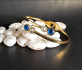 Gold bracelet with blue and clear gemstones on white stones against a dark background