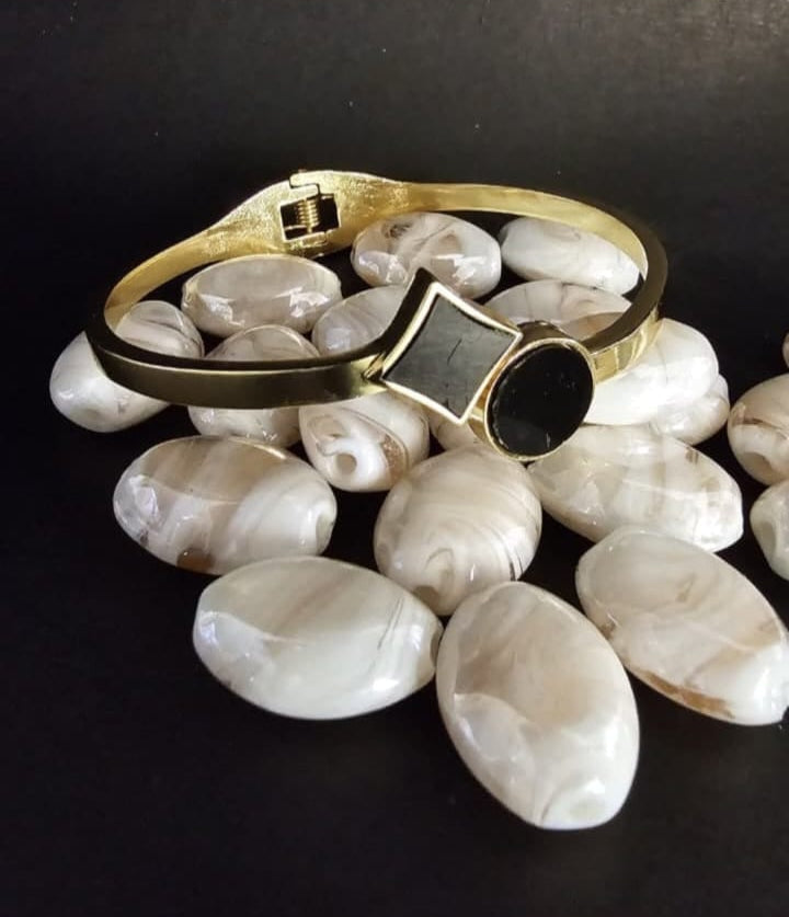 Gold bracelet with a black gemstone on a dark surface with white stones
