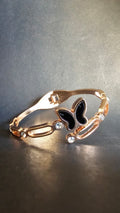 Rose gold bracelet with a black butterfly charm on a reflective surface