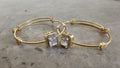 Gold bangles with square gemstones on a gray surface