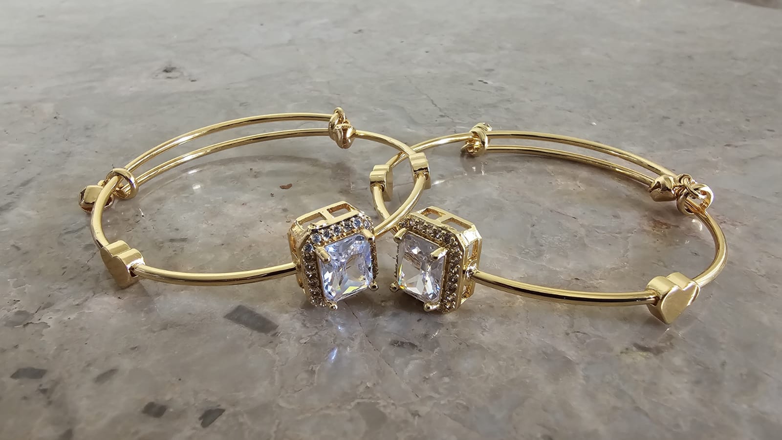 Gold bangles with square gemstones on a gray surface