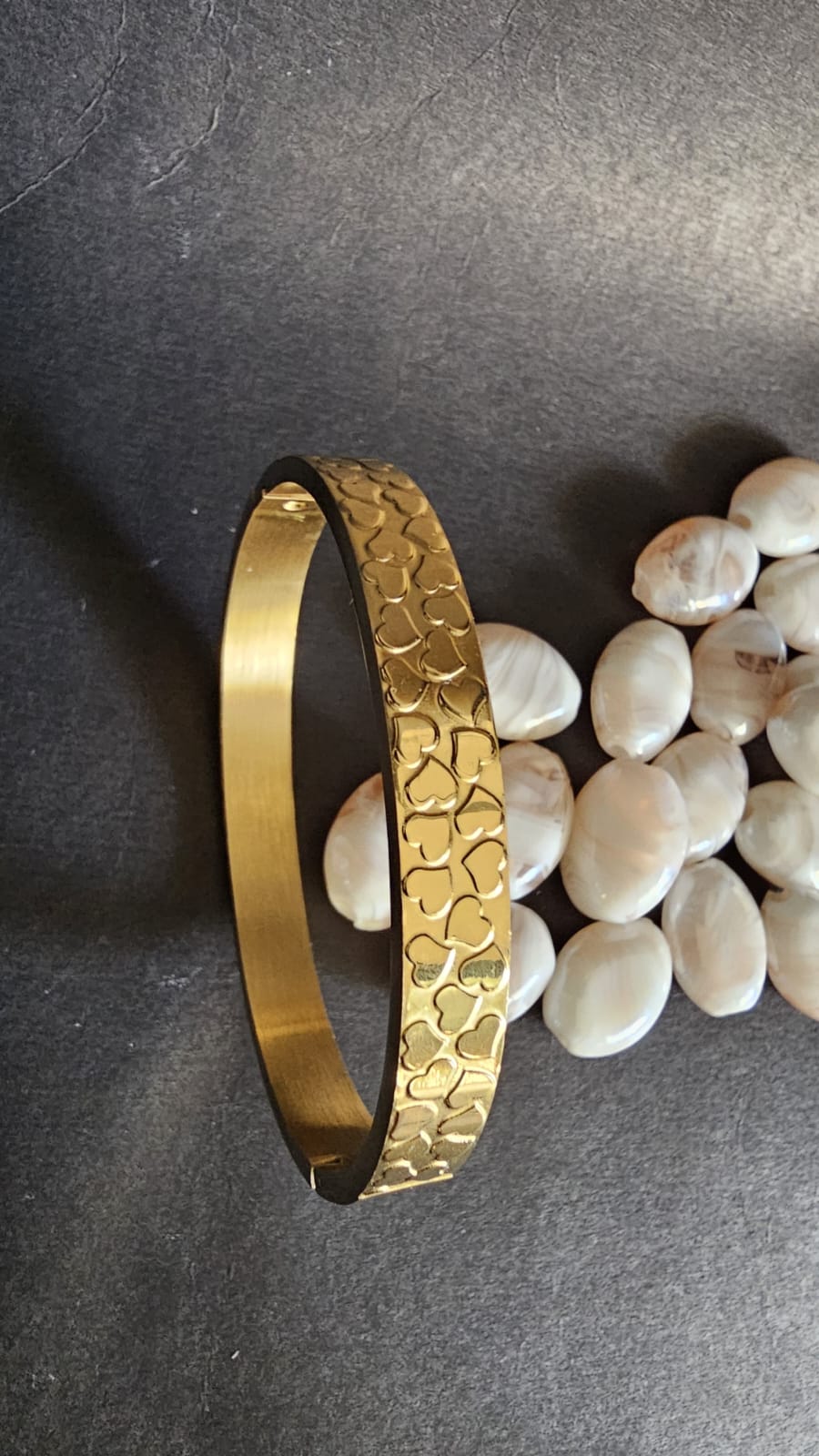 Gold bracelet with textured pattern on a dark surface with pebbles