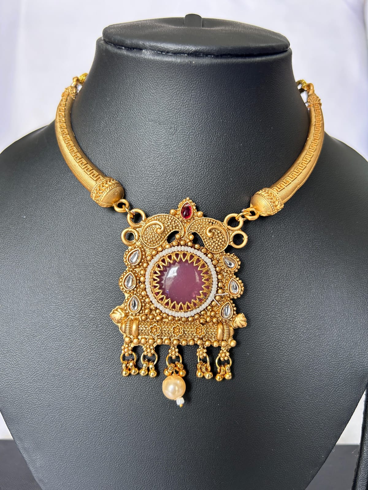 Gold necklace with a purple gemstone on a black mannequin