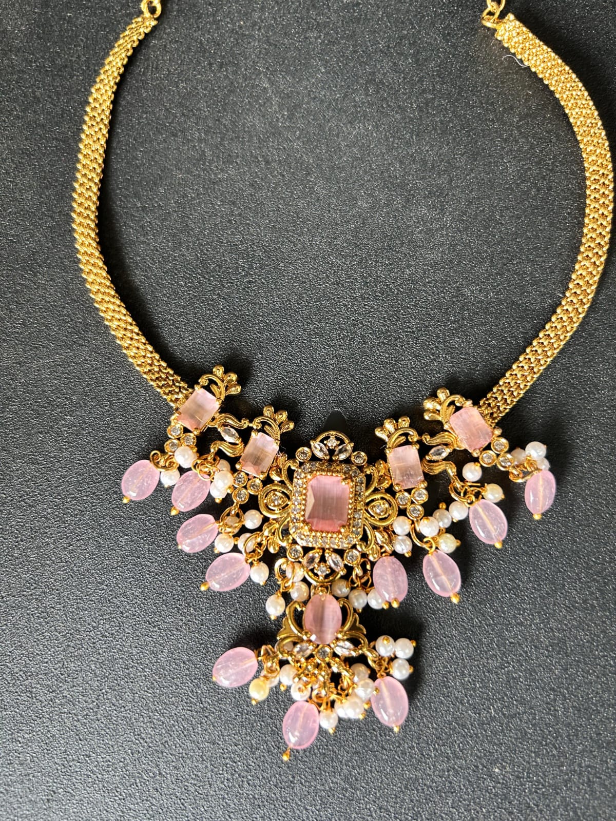 Gold necklace with pink gemstones on a gray background