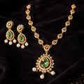 Gold necklace with green gemstones and pearl earrings on a black velvet background