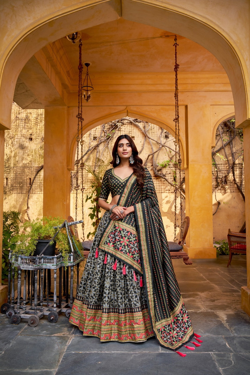 Woman in traditional black and gold embroidered outfit standing in a decorative outdoor setting.