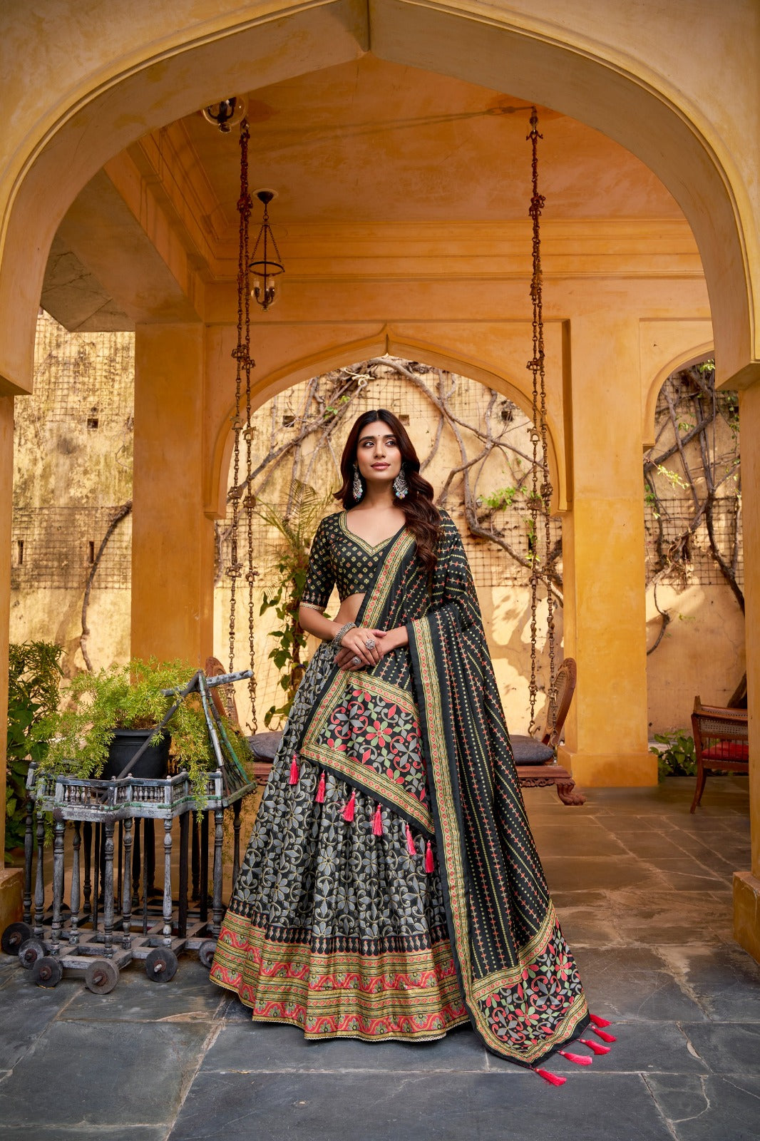 Woman in traditional black and gold embroidered outfit standing in a decorative outdoor setting.
