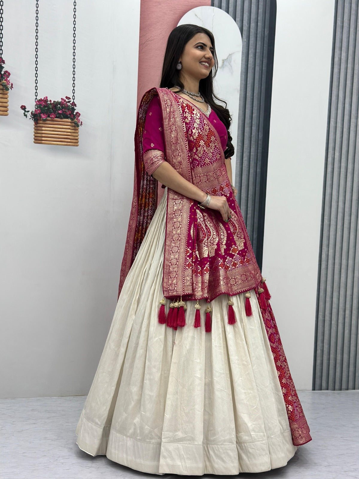 Woman in a traditional outfit with a white and red saree, standing indoors.