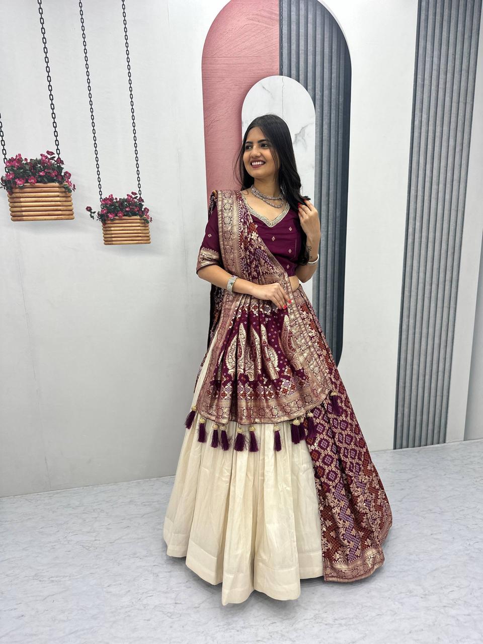 Woman in a traditional outfit standing in front of a mirror with a pink lamp and hanging plants in the background.