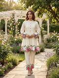 Woman in a cream embroidered outfit standing in a garden with flowers and a gazebo.