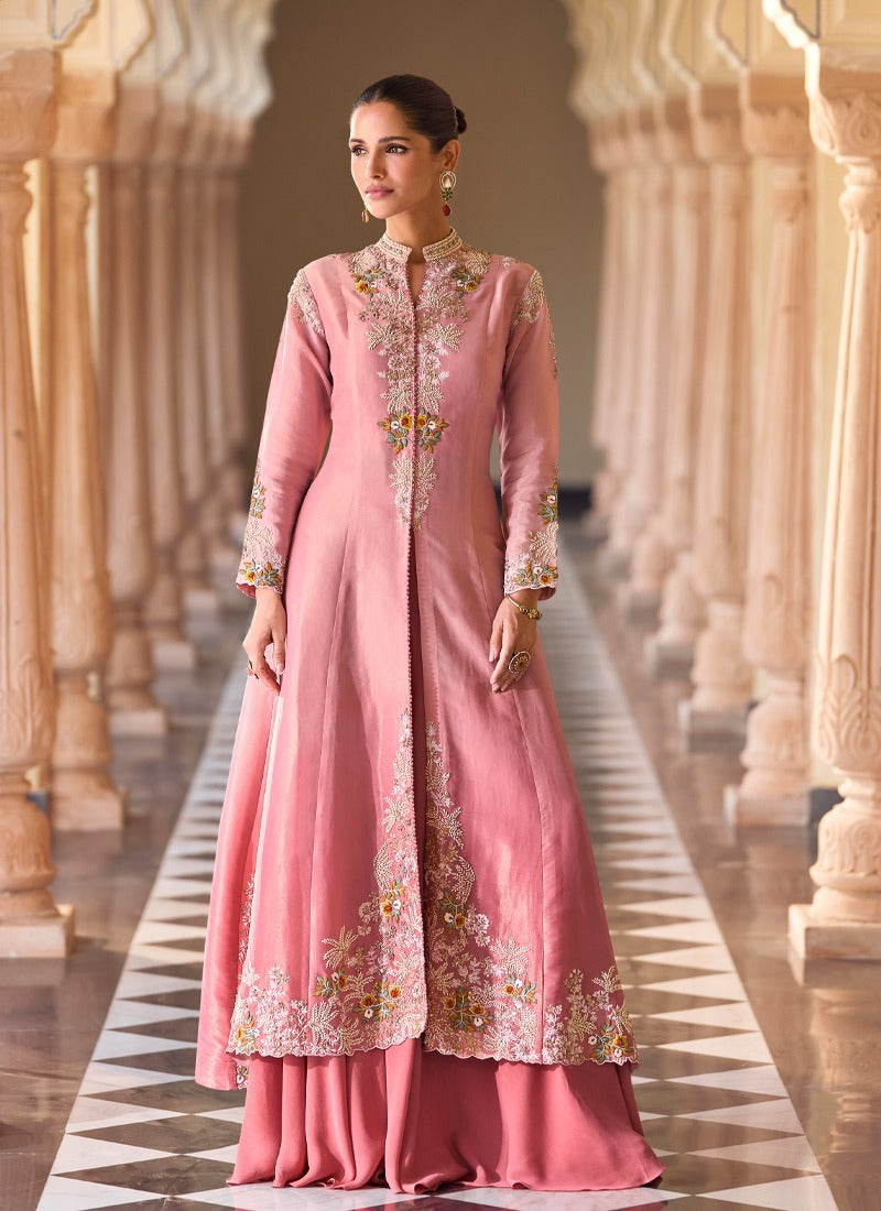 Woman in a pink embroidered traditional outfit standing in an architectural setting.