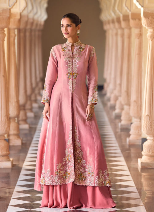 Woman in a pink embroidered traditional outfit standing in an architectural setting.