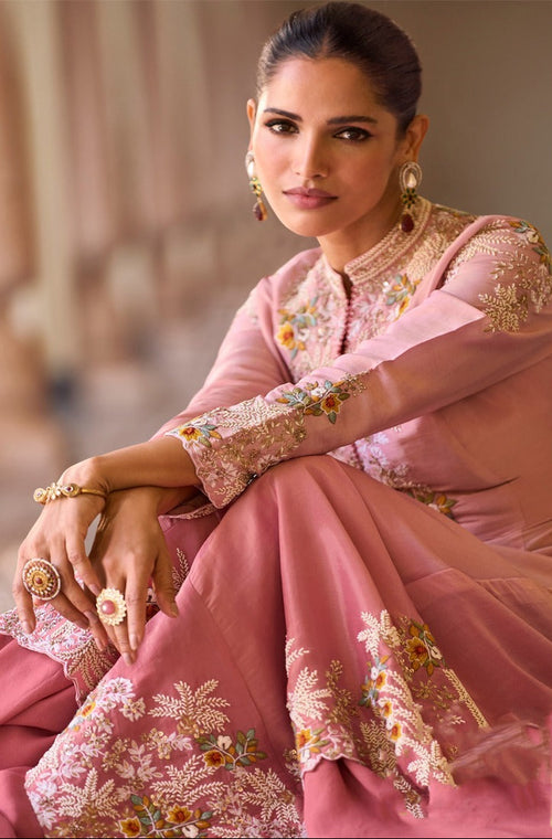 Woman wearing a pink embroidered traditional outfit with gold jewelry.